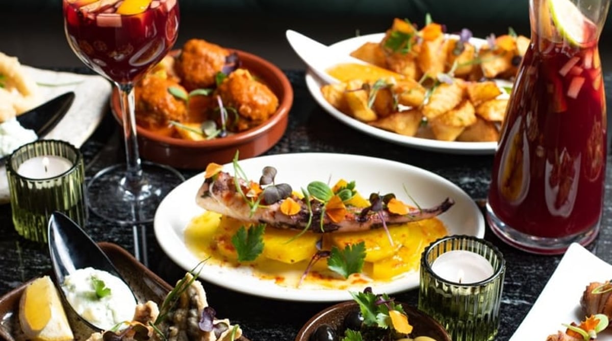 Sangría und mehrere Tapas auf einem dunklen Tisch vor einer grünen Sitzbank