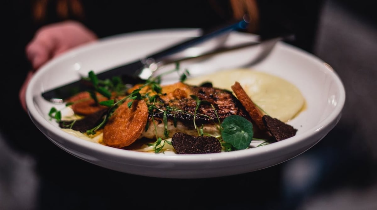 Teller mit Gemüse, Sauce und gebratenem Fleisch, von einer Hand serviert