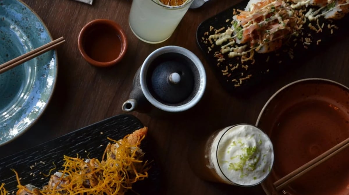 Gedeckter Holztisch im MOSTROS von oben mit Sushi-Rolls, Limonade, Teekanne und Cocktail