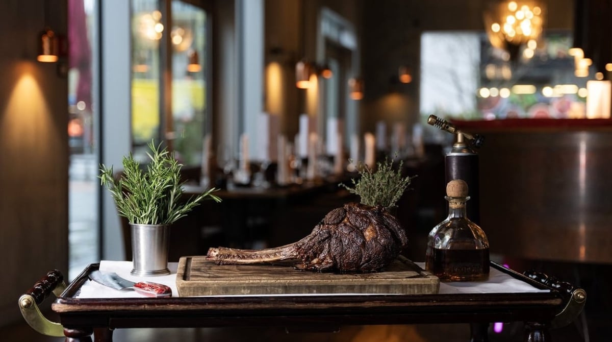 Großer Steak-Cut am Knochen mit Rosmarin auf dem Holzbrett am Servierwagen