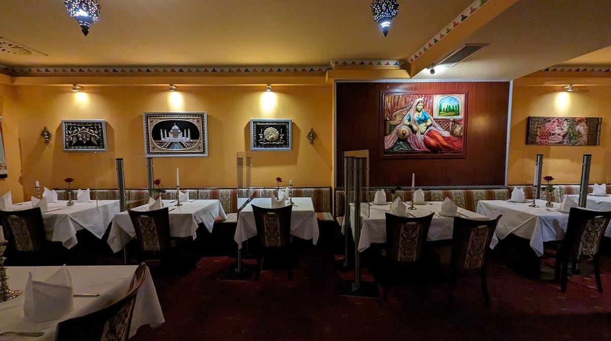 Gastraum des Taj Mahal mit weiß eingedeckten Tischen, gelben Wänden und Bildern mit indischen Motiven