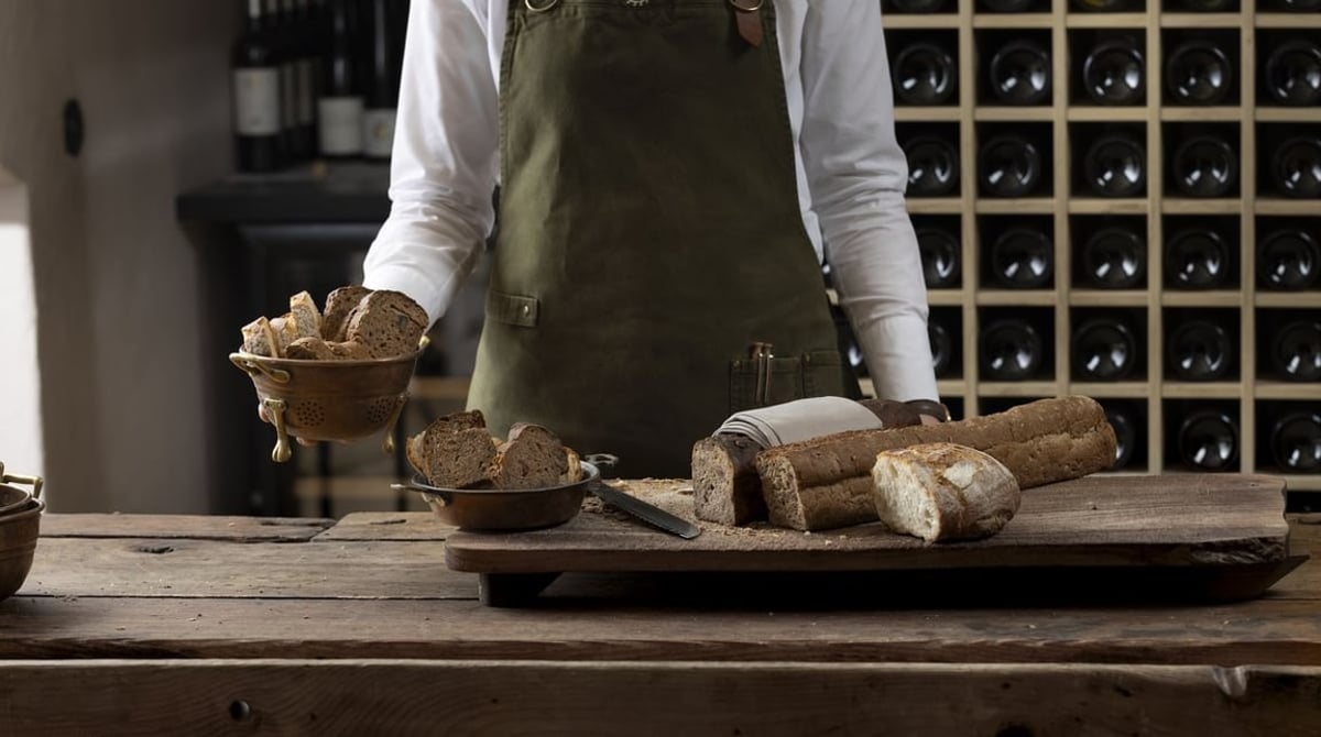Servicekraft mit Brot und Brotkorb vor einem Weinregal in der Pfistermühle