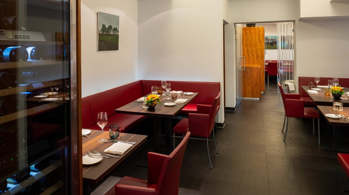 Durchgang im Restaurant Huber mit Weinklimaschrank, roten Stühlen und gedeckten Tischen