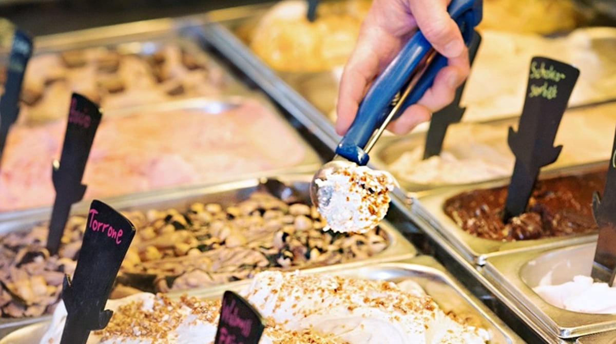 Eisvitrine mit Eisspachtel und Sorten mit Nüssen und Schokolade