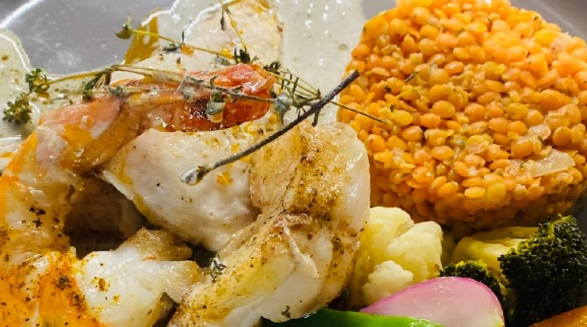 Gebratene Scampi mit Gemüse und einem Taler aus roten Linsen auf grauem Teller