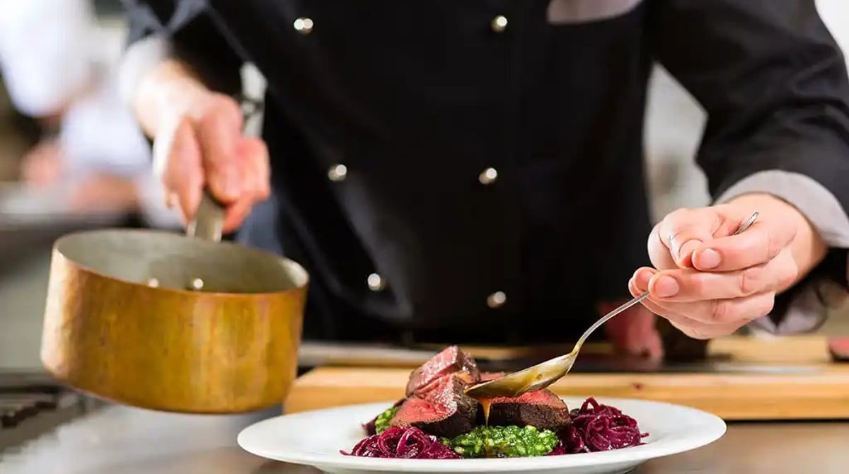 Küchenchef richtet rosa gebratenes Rinderhüftsteak mit Gemüse an