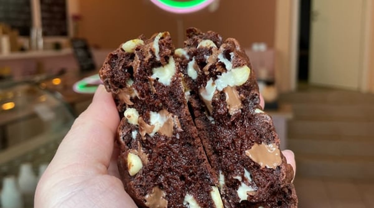 Hand hält einen aufgebrochenen Schoko-Cookie vor dem Dapkies-Neonschild