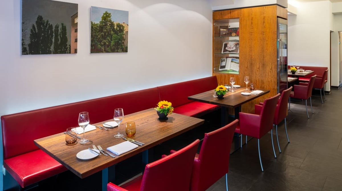 Gastraum des Restaurant Huber mit roter Bank, gedeckten Holztischen und Landschaftsbildern an der Wand