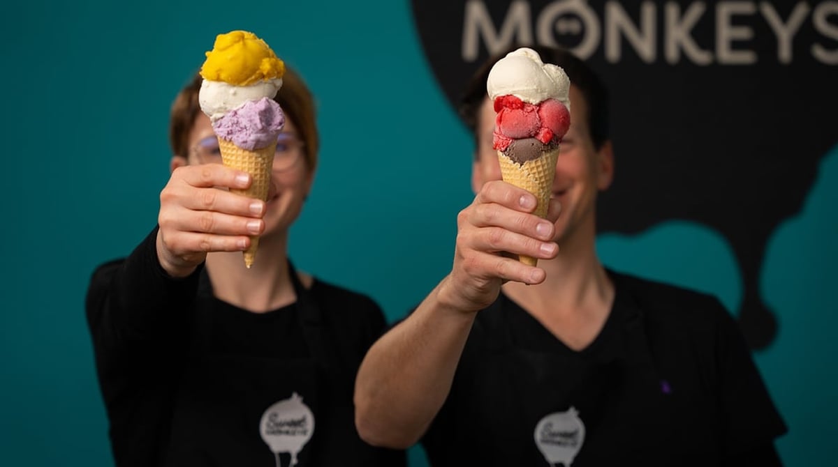Zwei Eiswaffeln mit mehreren Kugeln, davor das Sweet-Monkeys-Team vor türkisfarbener Wand