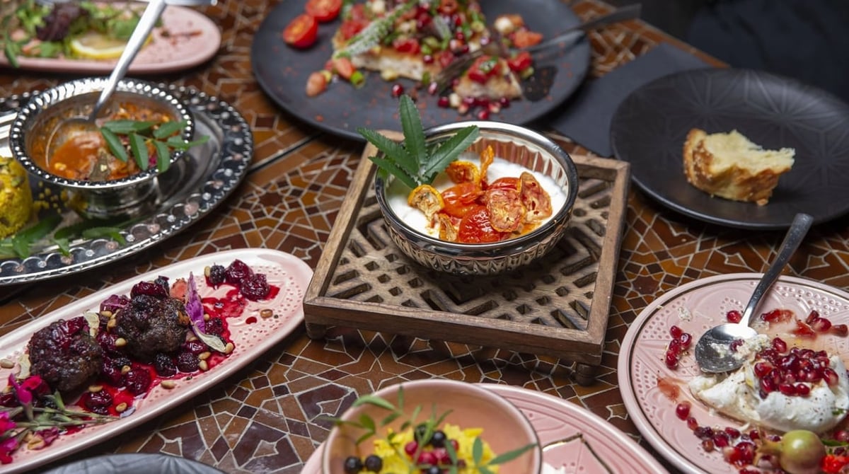 Tisch mit Mosaikplatte und vielen levantinischen Mezze auf rosa und dunklen Tellern