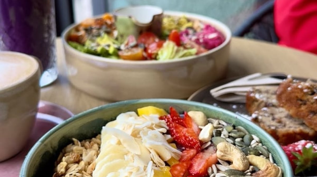 Açaí-Bowl mit Banane, Erdbeeren, Kokos und Nüssen, dahinter eine Buddha Bowl