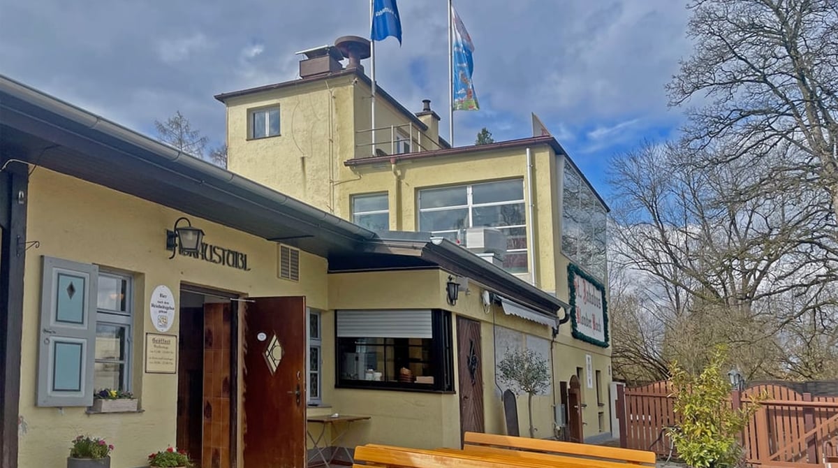 Außenansicht des Bräustüberls der Forschungsbrauerei in Perlach mit Biertischen und Fahnen vor dem gelben Brauereigebäude