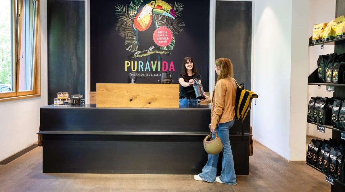Verkaufstresen im Rösterei-Laden mit Pura-Vida-Wandbild und Kaffeeregalen