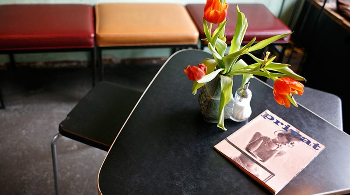 Kleiner Tisch mit Tulpen in einer Vase und einem Heft im Café Kosmos