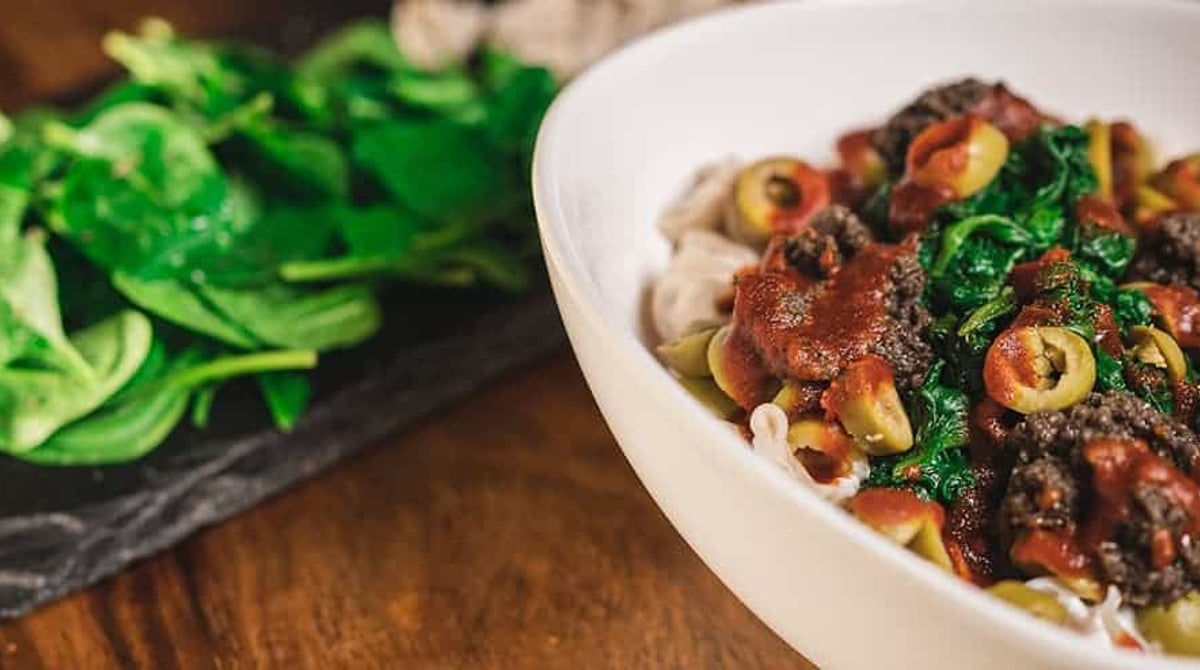 Schale mit Manti, Hackfleischsauce, Oliven und Spinat