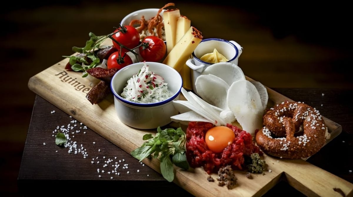 Wirtshaus-Brettl mit Obazda, Käse, Rindertatar und Brezn auf einem Holzbrett