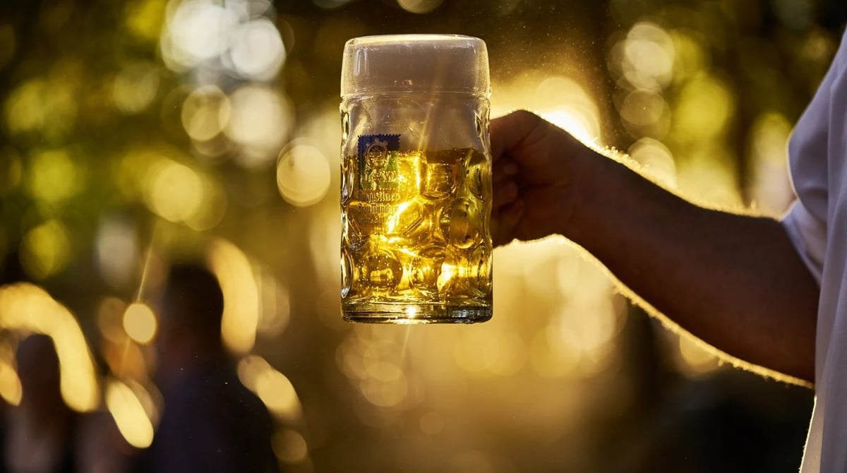 Hand hält eine Maß Bier im Gegenlicht vor dem Biergarten
