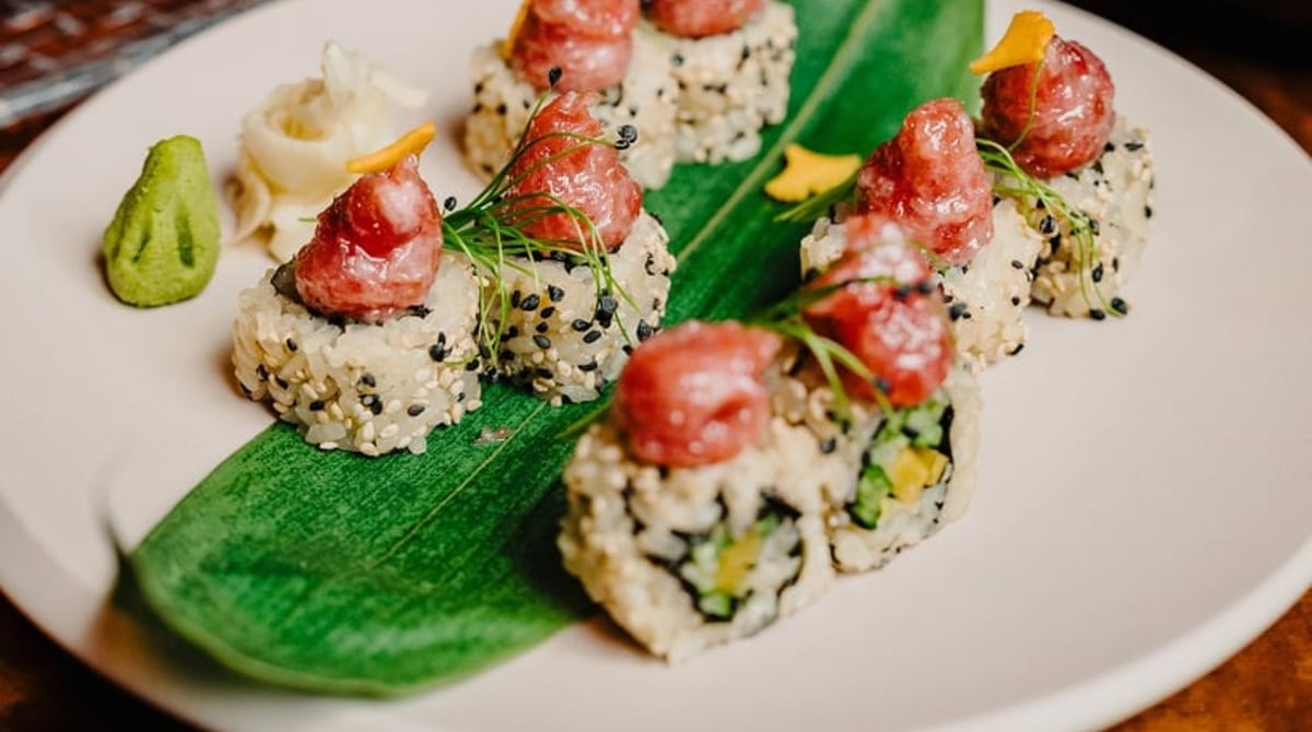 Teller mit rot belegten Sushi-Rollen in Sesam auf einem grünen Blatt, daneben Wasabi und Ingwer, im Koi am Wittelsbacherplatz