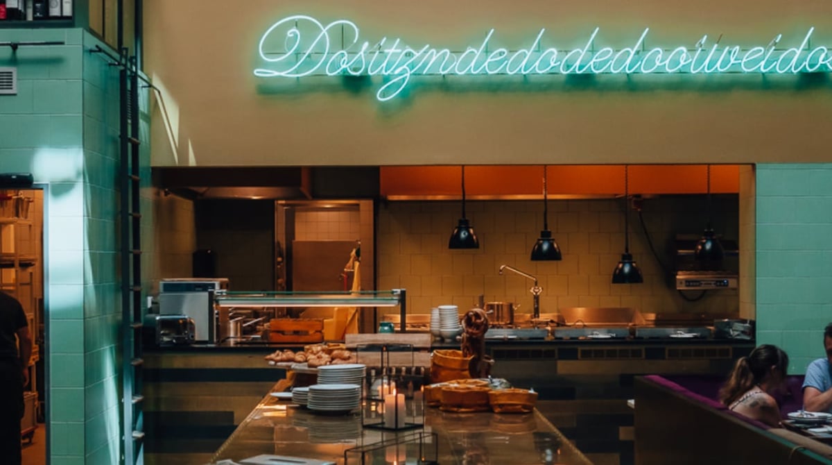 Offene Küche und Gastraum des NENI im 25hours Hotel The Royal Bavarian in München, darüber eine Neon-Schrift