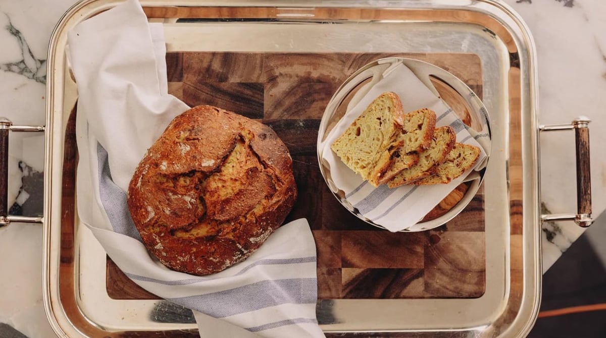 Rundes Brot auf einem Holzbrett und Brotscheiben auf einem Teller, serviert auf einem Silbertablett