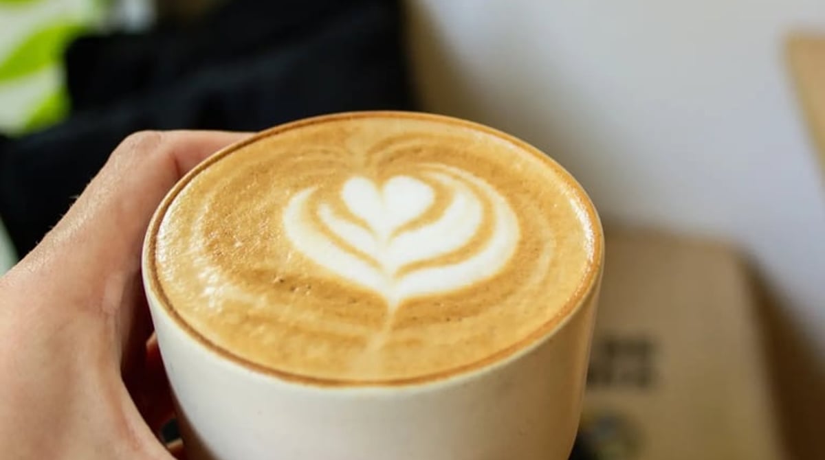 Hand hält eine Tasse Latte mit Herzmuster im Milchschaum
