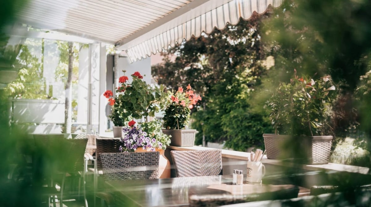 Terrasse der Taverna Naxos mit Markise, Blumen und gedeckten Tischen
