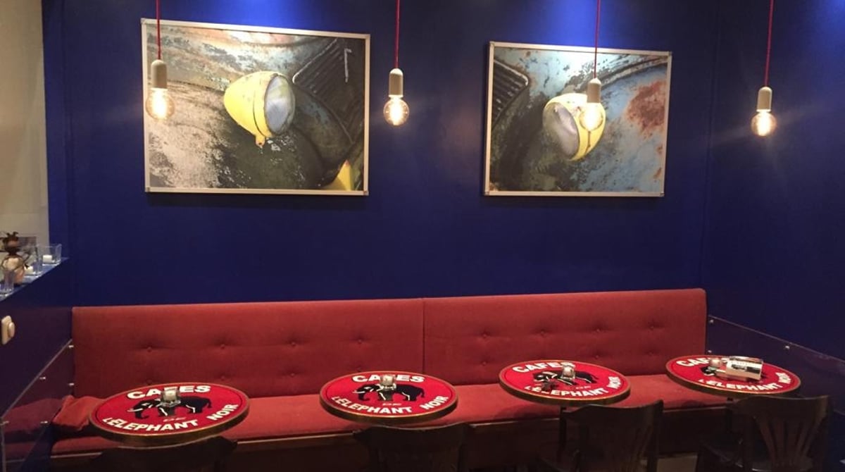 Gastraum des Le Faubourg mit roter Polsterbank, runden Bistrotischen und Bildern an dunkelblauer Wand