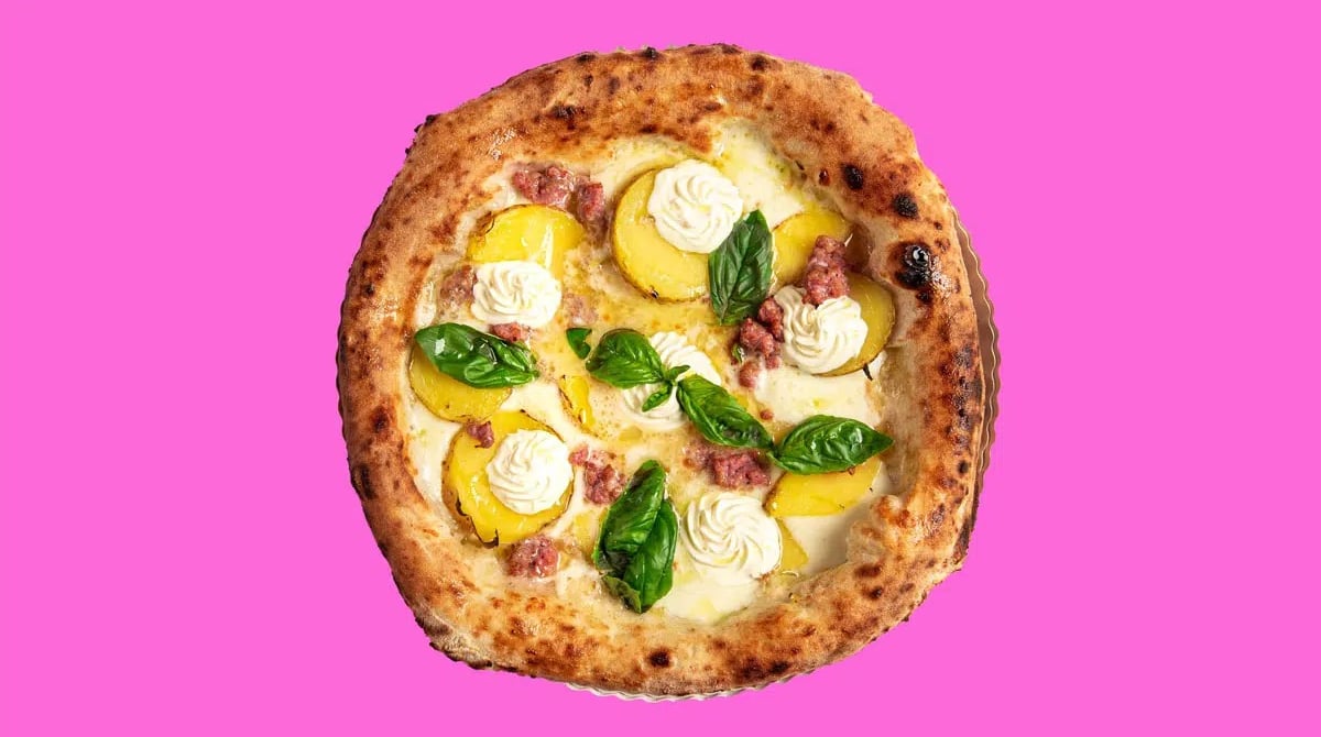 Pizza mit Wurststückchen, Basilikum und weißen Cremetupfen auf pinkem Hintergrund