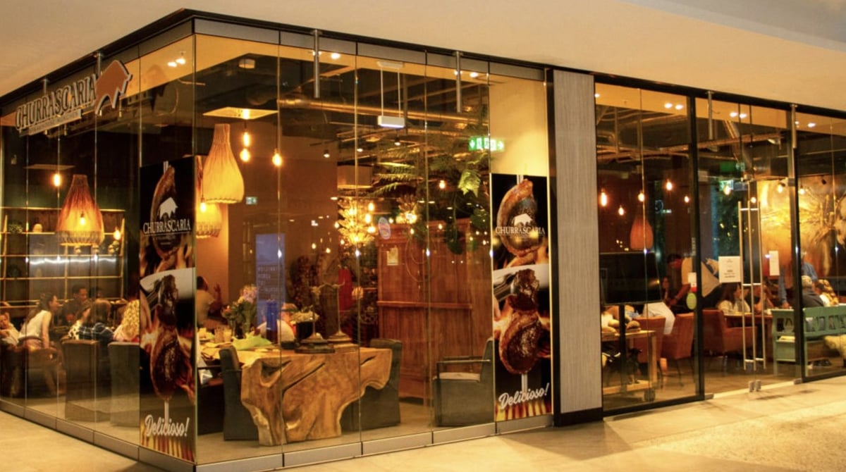Glasfront der Churrascaria im Forum Schwanthalerhöhe mit Schriftzug, Stier-Logo und Blick auf gedeckte Tische