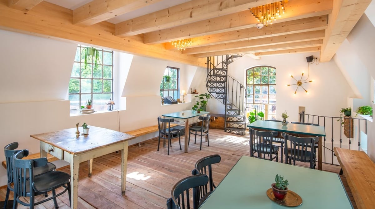 Heller Dachspitz im zweiten Obergeschoss des Gans Woanders mit Holztischen und Wendeltreppe
