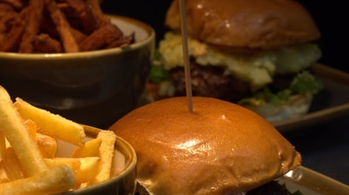 Zwei Burger mit Pommes und Süßkartoffelpommes auf dunklen Tellern
