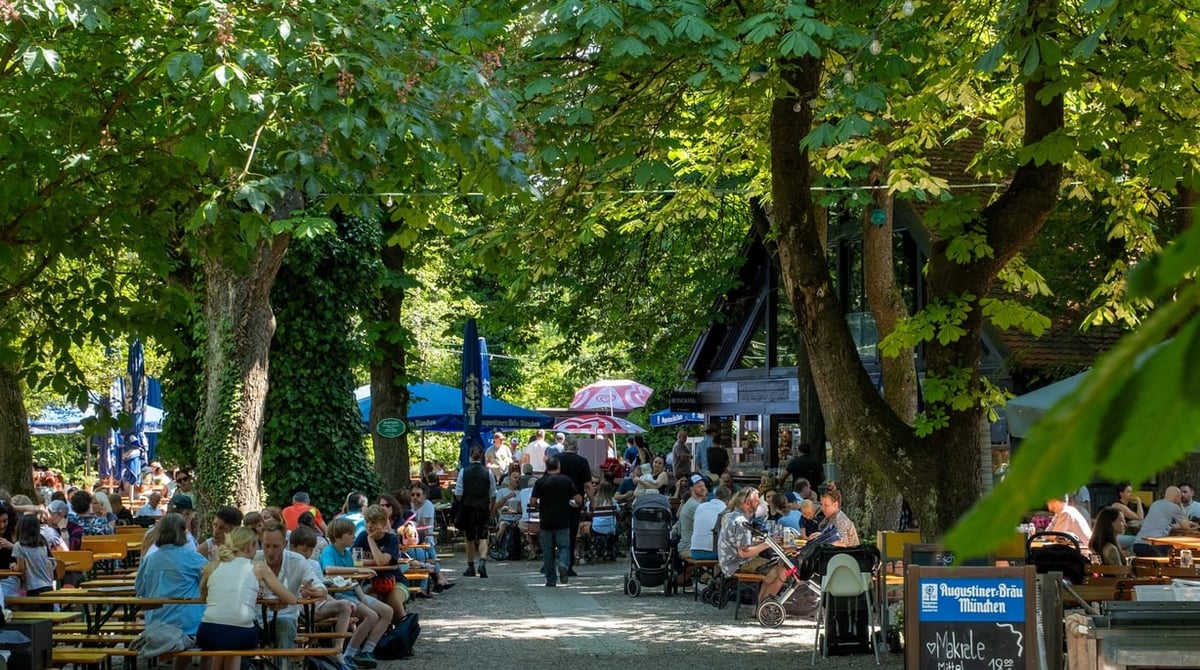 Kiesweg zwischen Biergartentischen unter hohen Bäumen im Biergarten der Insel Mühle in Untermenzing