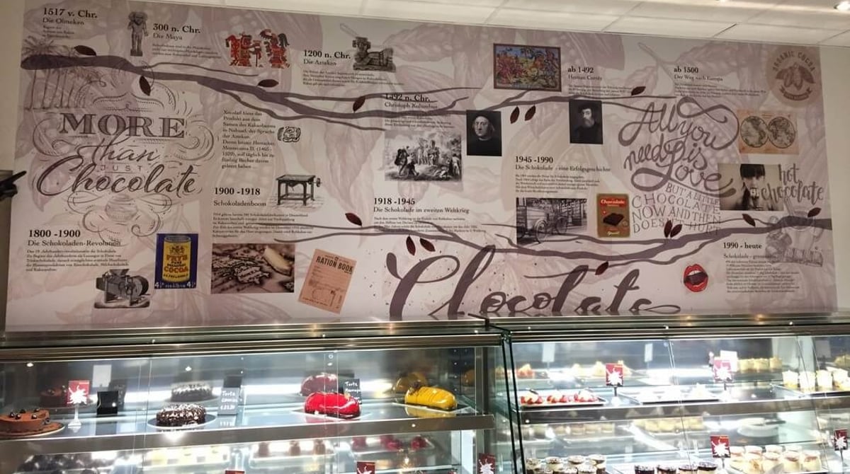 Vitrine mit Törtchen vor der Wand mit dem Schriftzug „More than Chocolate" im ChocoLab