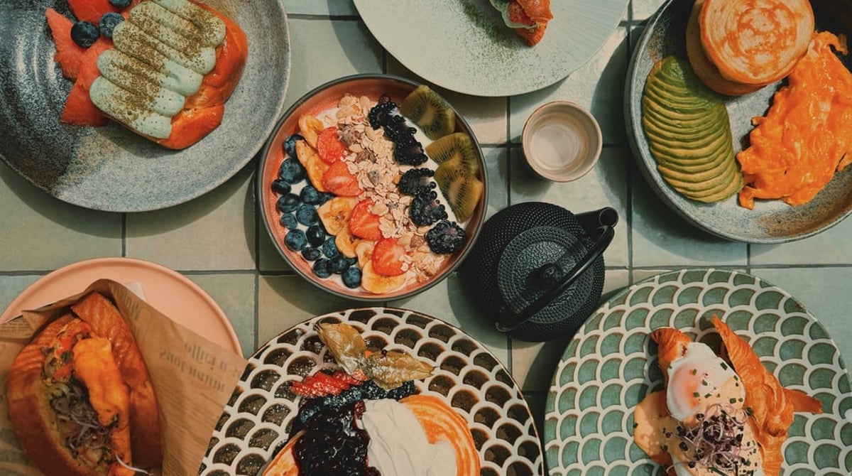 Brunch-Gerichte mit Pancakes, Bowls und Croissant auf bunten Tellern, von oben fotografiert