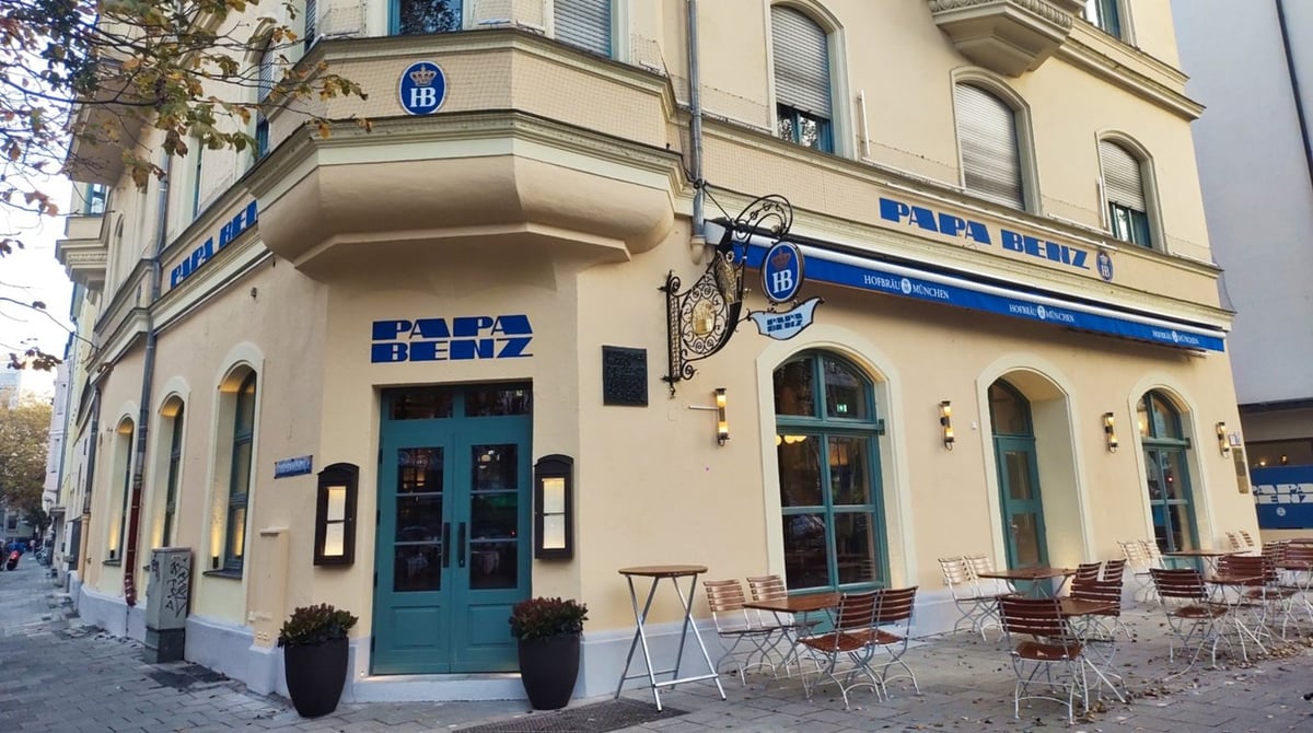 Das Papa Benz an der Ecke Leopoldstraße in München-Schwabing mit blauem Schriftzug, Hofbräu-Markise und Tischen vor dem Haus