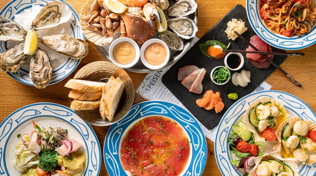 Gedeckter Tisch mit Austern, Bouillabaisse, Sashimi, Salaten und Baguette in blau-weißem Geschirr