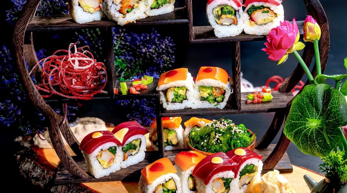 Vegane Sushi-Rollen auf einem kleinen dunklen Holzregal mit Lotusblüten im Padme Hum