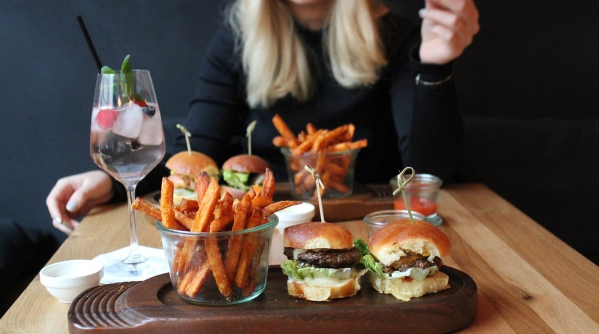 Mini-Burger, Süßkartoffel-Pommes und ein Drink auf einem Holztisch