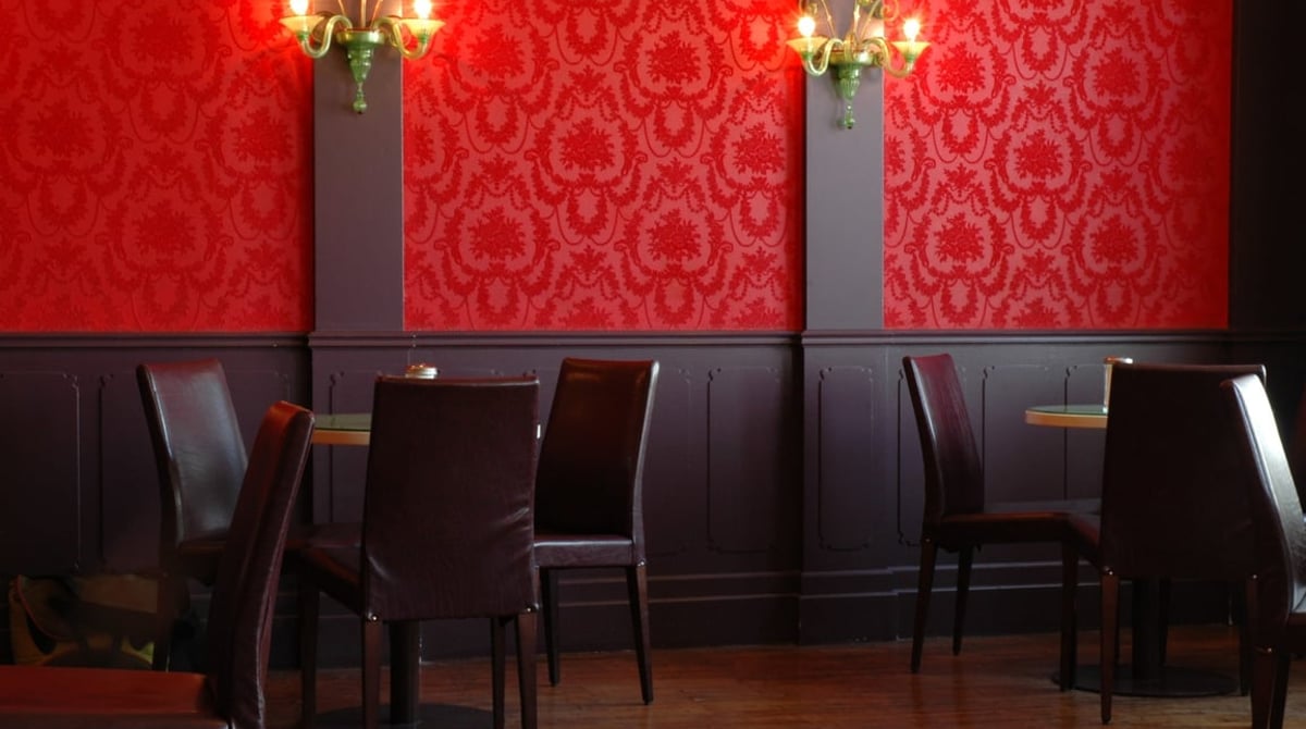 Raum mit roter Tapete, Wandleuchten und dunkler Holzvertäfelung im Cafe Glockenspiel