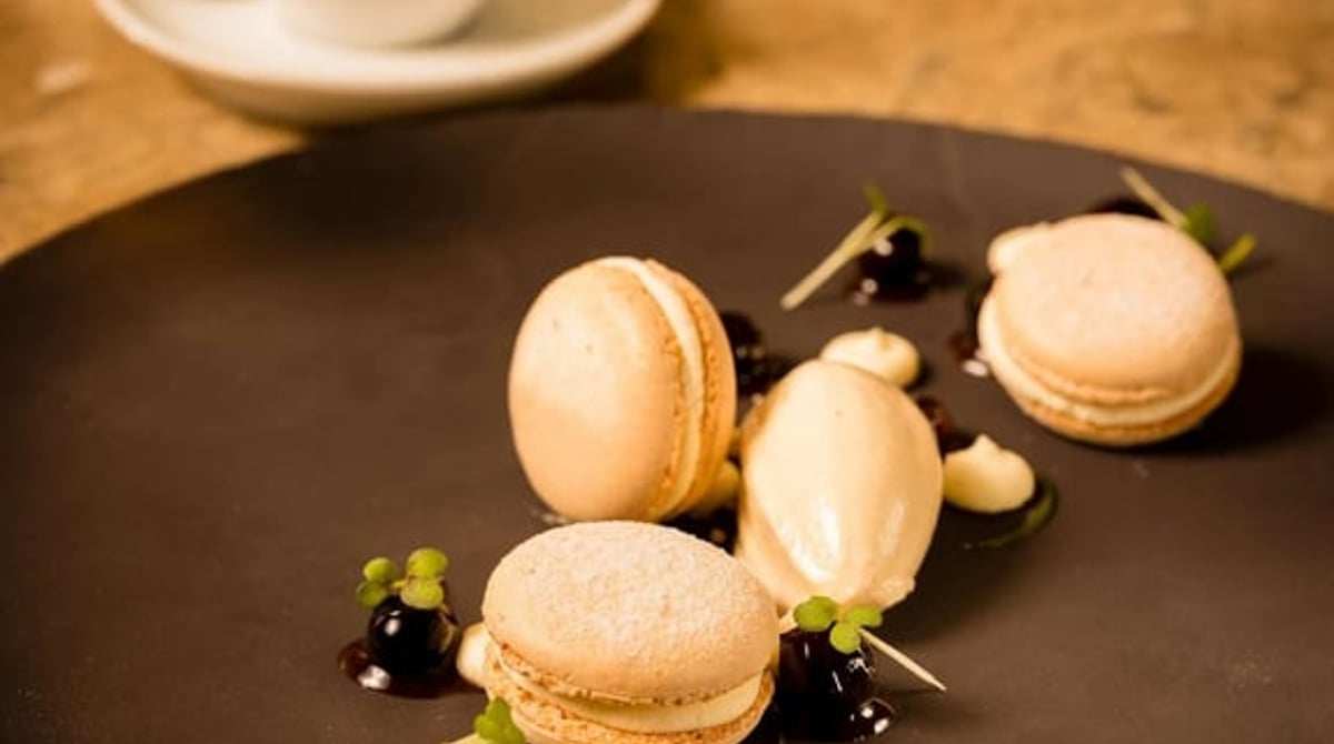 Macarons mit Beeren auf einem dunklen Teller, davor eine Espressotasse