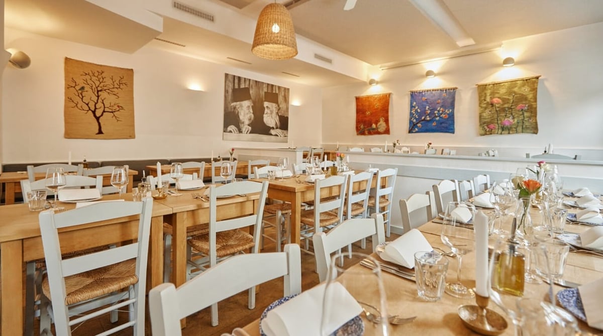 Gastraum der Taverna Paros mit Holztischen, weißen Stühlen und bunten Wandbildern
