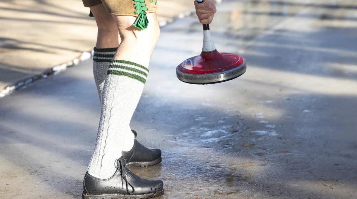Eisstockschütze in Lederhose und Trachtenstrümpfen auf der Eisbahn im Königlichen Hirschgarten