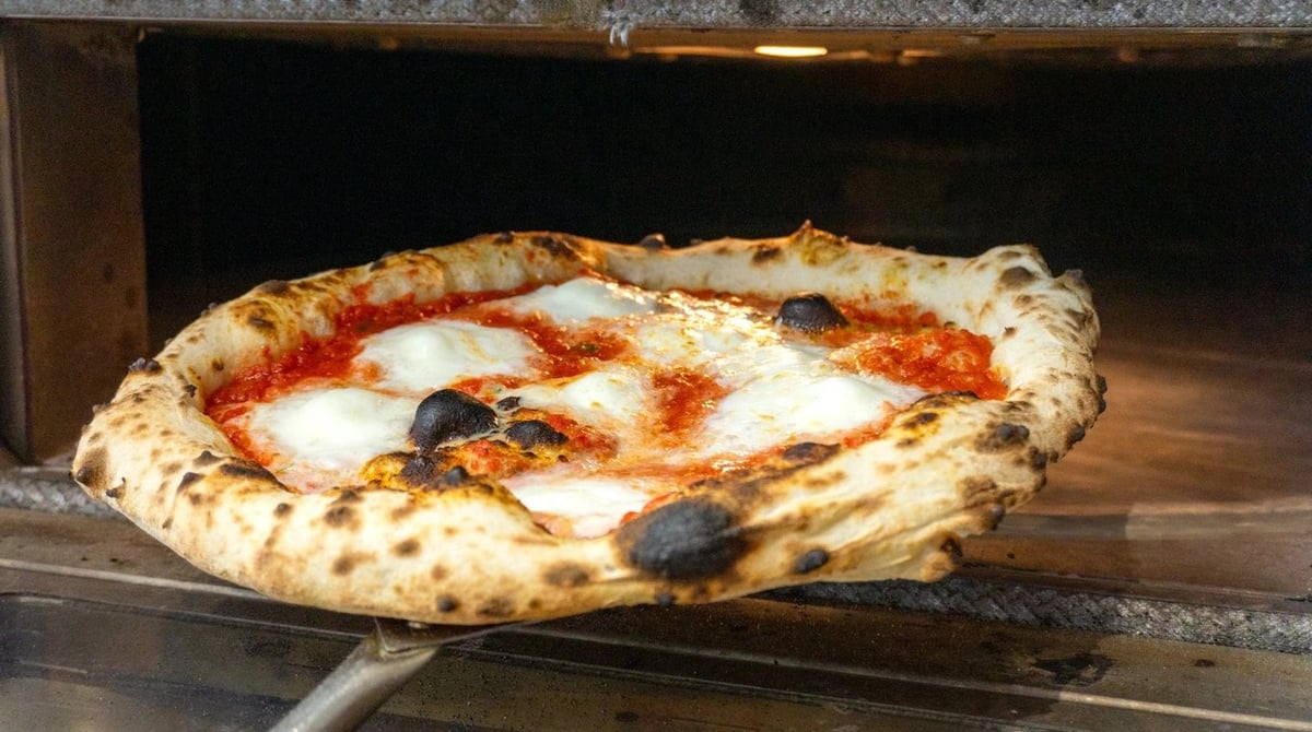 Neapolitanische Pizza mit Mozzarella und Basilikum auf der Pizzaschaufel vor dem Ofen