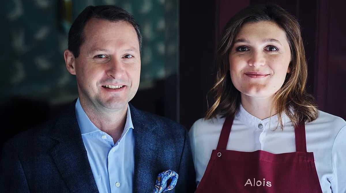 Zwei Mitglieder des Alois-Teams vor der Kranich-Tapete, die Frau in roter Alois-Schürze