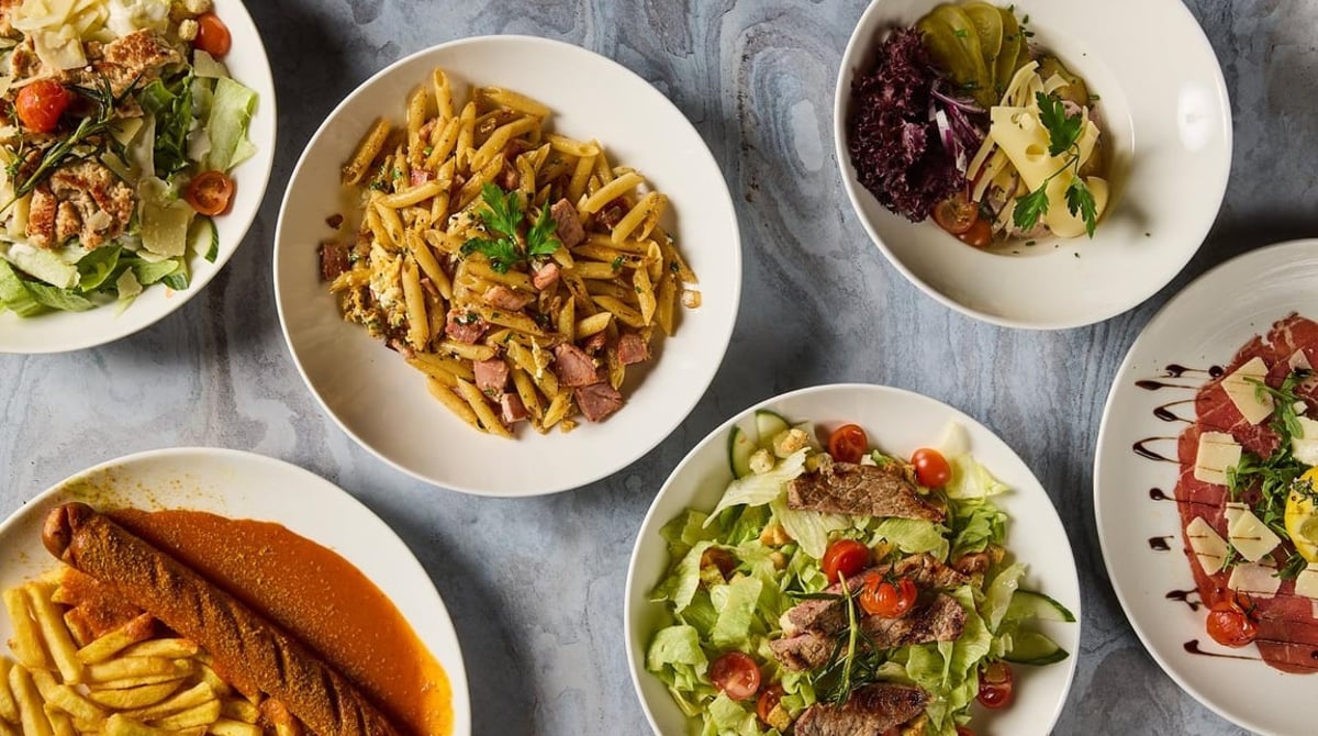 Teller mit Salaten, Pasta und Currywurst mit Pommes von oben fotografiert