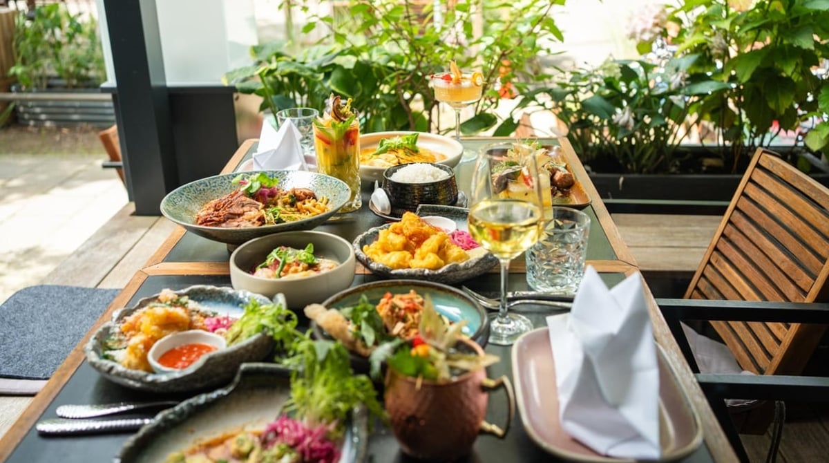 Vietnamesische Gerichte und Weißwein auf einem Tisch zwischen Pflanzen im Rice Garden