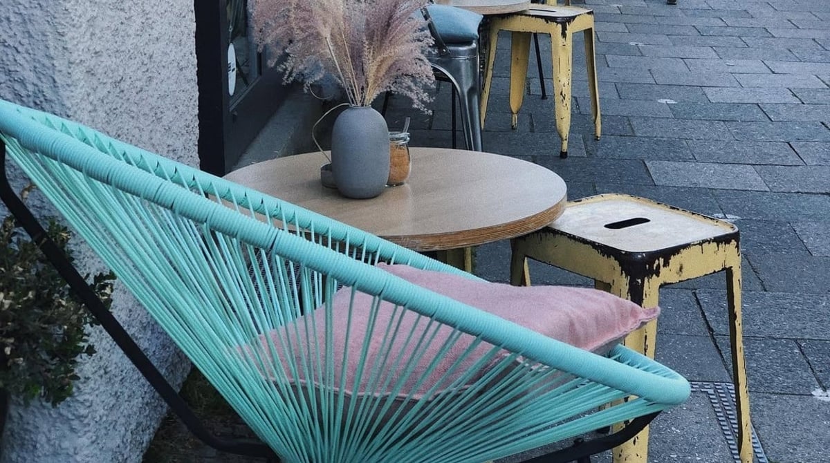 Türkiser Korbsessel, runder Holztisch mit Vase und gelber Hocker vor dem Café Daddy Longlegs in der Barer Straße