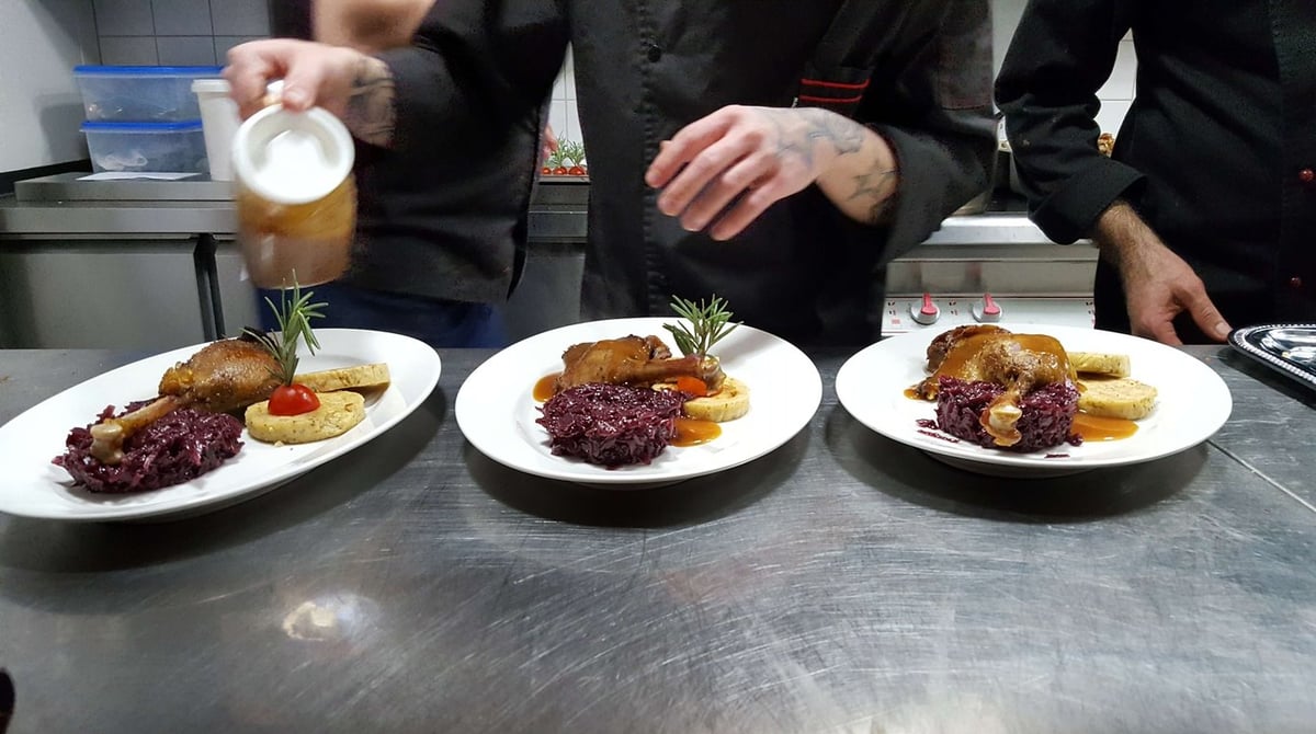 Drei angerichtete Teller mit Entenkeule, Rotkohl und Knödel in der Küche