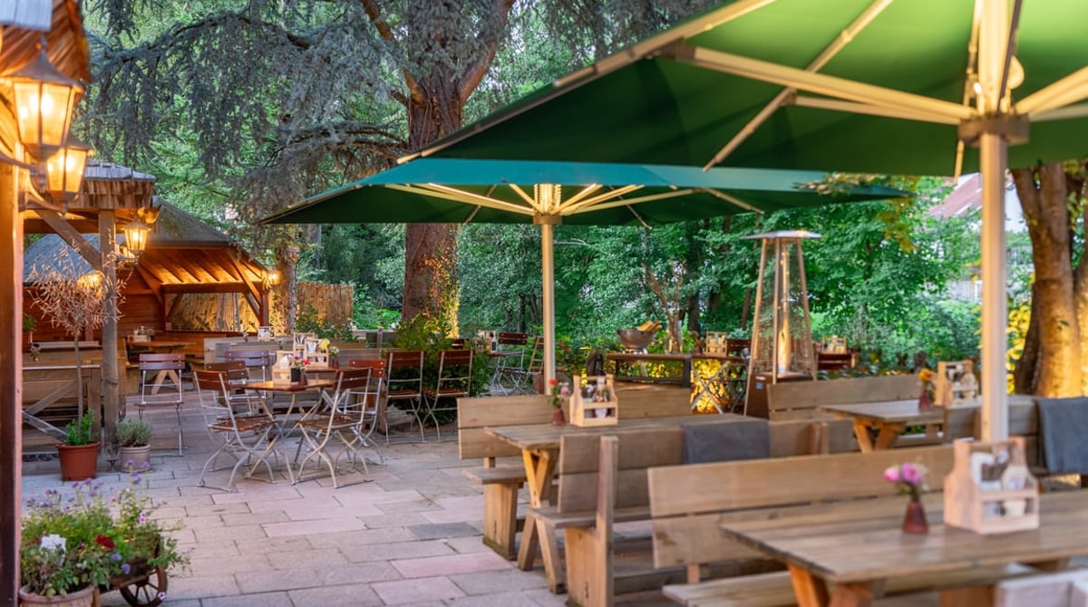 Terrasse der Pablo Emilio BurgerBar mit grünen Sonnenschirmen, Holzbänken und Bäumen an der Würm