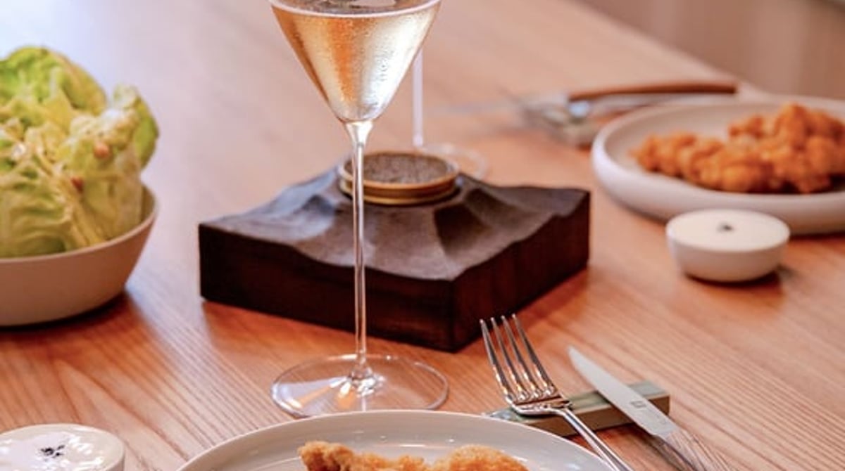 Kalbsschnitzel und Salat auf einem Holztisch mit zwei Gläsern Champagner